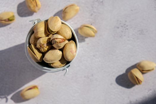 Pistachios in white bucket on concrete background. Healthy and dietary nutrition. Concept of nuts. Vegan protein omega vitamin food.