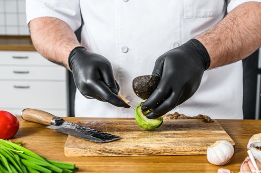 A chef in black gloves prepares guacamole from fresh avacado Hass