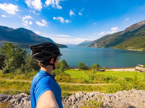 Theme of mountain biking in Scandinavia. human tourist in helmet and sportswear on bicycle in Norway on Hardanger Bridge suspension bridge thrown across the Hardanger Fjord in southwestern Norway
