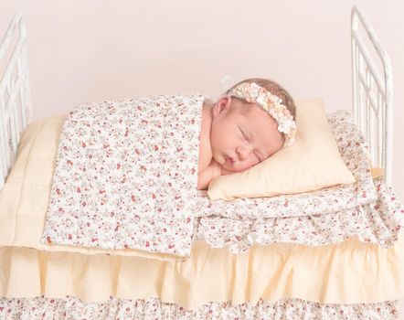 Infant in hairband napping under the sheets