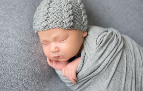 Newborn baby sleeping curled up in grey blanket