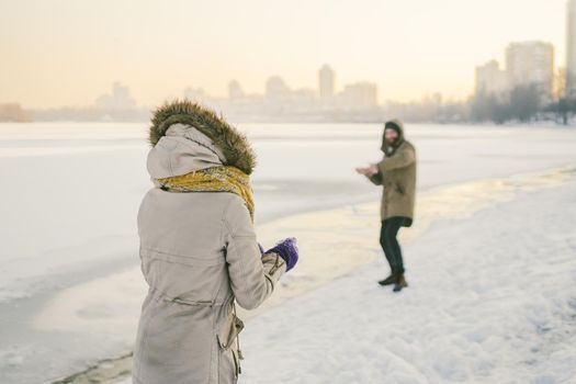 Young Caucasian people in love heterosexual couple have a date in winter near a frozen lake. Active holiday holiday Valentine's Day, playing snowballs and playing joy