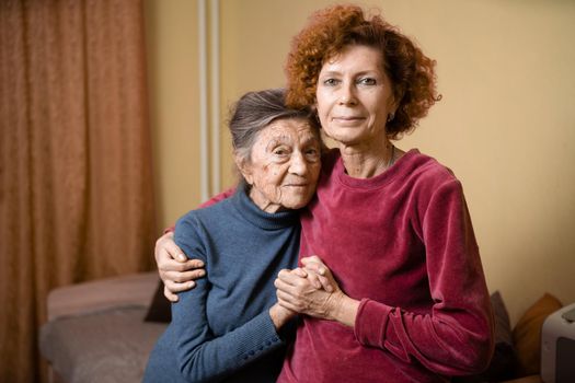 Adult daughter takes care of elderly mother suffering from dementia, old woman ninety years age gray hair and wrinkles on face and sweet kind smile, family idyll caring for elderly, hug each other
