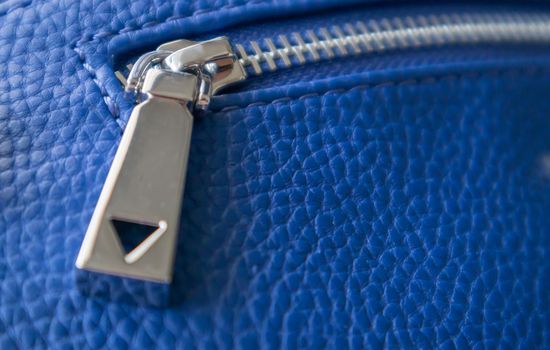 Natural or artificial leather texture. Fragment of a blue bag with a zipper and stitching. Zipper or clasp bag design element. Bovine skin texture with snake. Macro photo, selective focus.