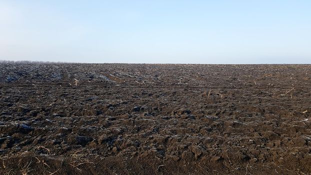 Agricultural field plowed by tractors under blue sky. The field has been plowed, crops have been sown. Close up of soil texture. Rural scene. Farming and food industry. Arable land of chernozem.