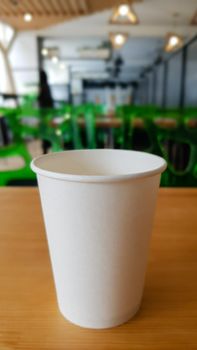 Paper white coffee cup disposable to take or go, on the wooden table of the coffee shop or dining room, place for a designer layout. Hot coffee cup in a cafe.