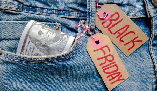 Money dollars in a lot in jeans pocket and cardboard tag with text black friday. Blue background, holiday concept. Black Friday - International day of purchases, promotions, discounts, sales. The sales season is the fourth Thursday of November. Copy space, place for text, flat lay
