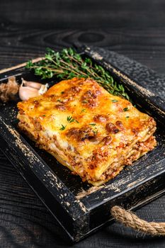 Portion of Lasagna with mince beef meat and tomato bolognese sauce in a wooden tray. Black wooden background. Top view