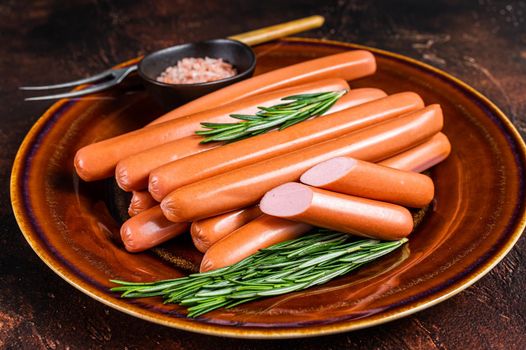 Frankfurter raw sausages in a rustic plate with herbs. Dark background. Top view
