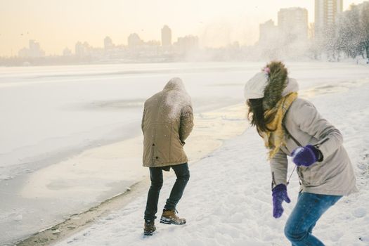Young Caucasian people in love heterosexual couple have a date in winter near a frozen lake. Active holiday holiday Valentine's Day, playing snowballs and playing joy