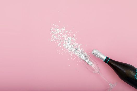 Bottle of champagne and glass on pink table with glitter