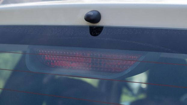 Rear window of a dusty white car with a stoplight behind glass, close-up. Red signals indicating vehicle braking. They turn on automatically when you press the brake and turn off when you release it.