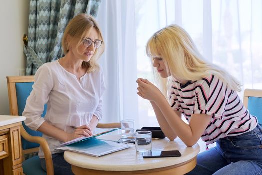 Female psychologist working with sad upset teenage girl, session in office