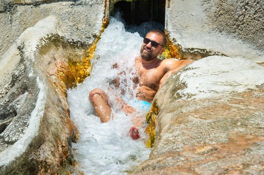 A man with glasses sits under a waterfall of healing water with thermal springs in Pamukkale.Turkey