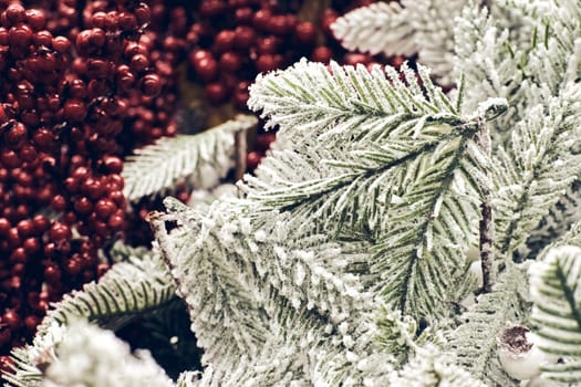 Christmas holiday decorations. Christmas fir tree brunch with red berries and cones in snow sparkling close up texture. Shallow focus. Christmas wallpaper concept