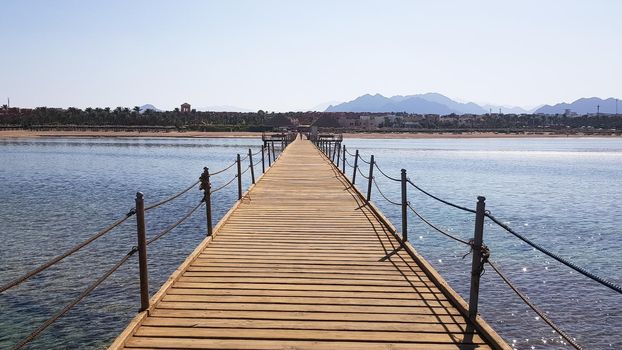 Long pontoon on the Red Sea in Egypt. Pontoon for descent into the water. Wooden bridge on the territory of the Amway Hotel in Sharm El Sheikh with metal fences and a rope over the sea with waves