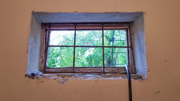 A rectangular basement window is tightened with a metal mesh and a grill. Technical window in the wall of an old gray building.