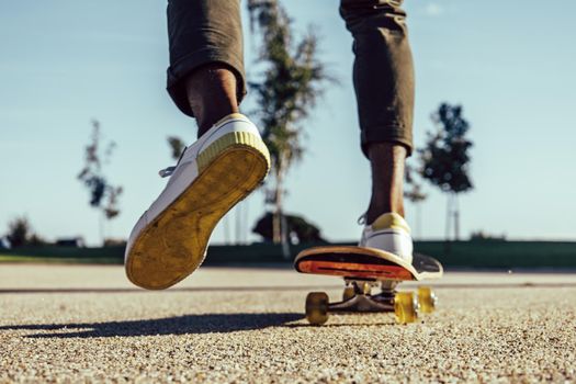 Closeup of dark skin legs riding skateboard in park