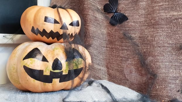 Pumpkin with a scary face on a wooden table. The interior of the house is decorated with pumpkins and spider webs for the holiday of Halloween.