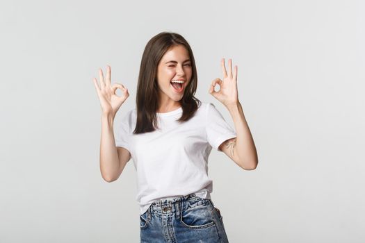 Satisfied cheerful brunette girl winking sassy and showing okay gesture in approval