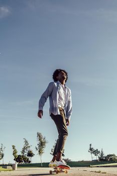 Young black ethnicity man with afro hair skateboarding and looking up to the sky