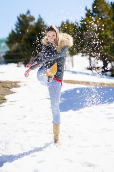 Young happy woman kicking snow in a snow-covered forest in the mountains