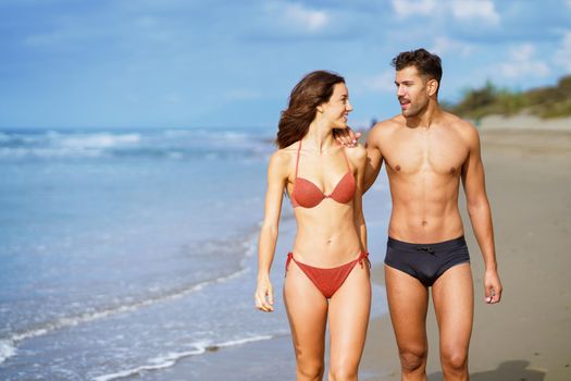 Young couple of beautiful athletic bodies walking together on the beach