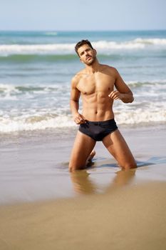 Handsome man on his knees on the sand of the beach