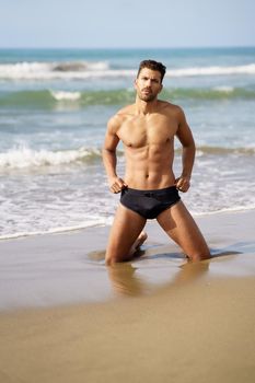 Handsome man on his knees on the sand of the beach