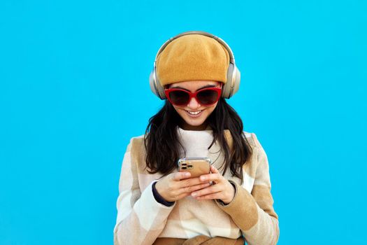 Cheerful woman in headphones browsing smartphone blue background
