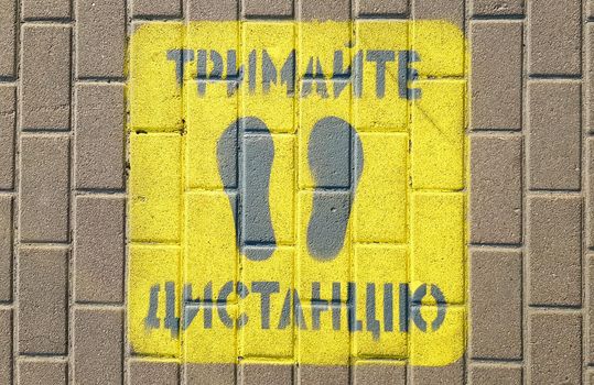 Ukraine, Kiev - April 23, 2020. Yellow sidewalk with the warning Keep your distance on the sidewalk. The text is in Ukrainian. Concept of maintaining social distance, quarantine or isolation