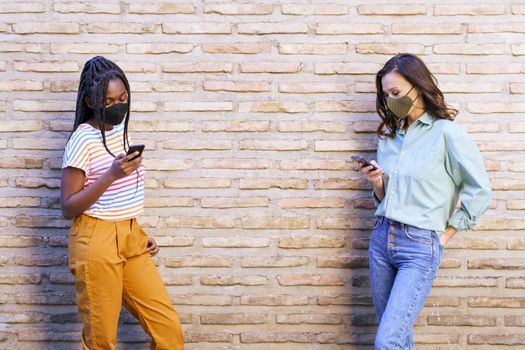 Multiethnic young women wearing masks using smartphone separated to respect social distance.