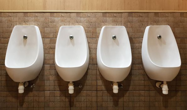 Four urinals lined up on the tiled wall of a modern men's public toilet, no privacy.