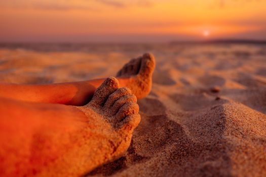 View of female barefoot legs on beach sand at sunset.