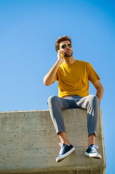 Young man using his smartphone sitting on a ledge outside
