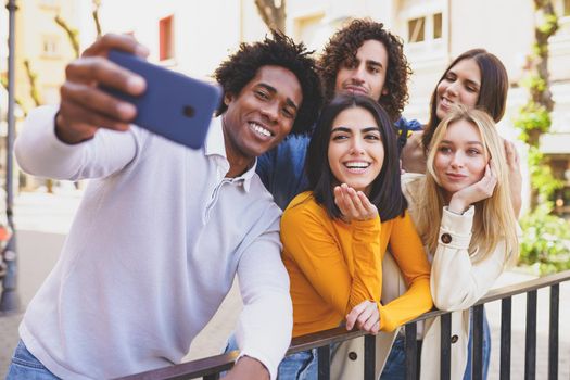 Black man with afro hair taking a smartphone selfie with his multi-ethnic group of friends.