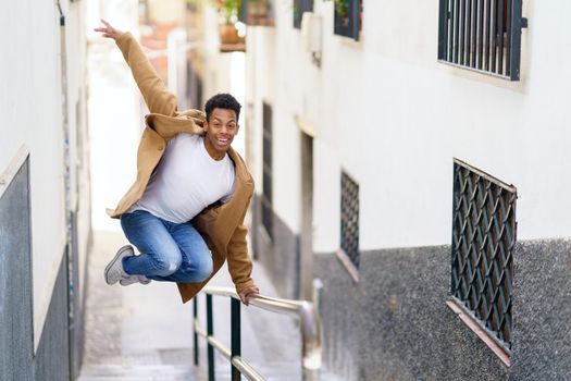 Young black man jumping for joy over a handrail in the street.