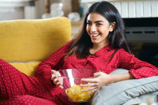 Persian woman at home watching TV eating chips potatoes