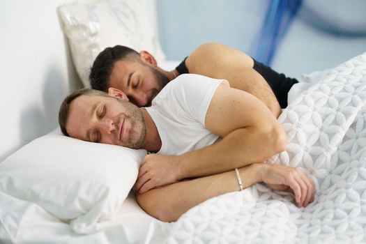 Gay couple sleeping together hugging in bed.