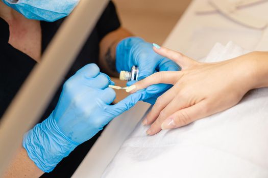 Close-up of Beautician painting her client's nails in blue and yellow nail varnish.