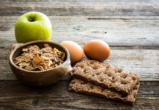 fitness breakfast with eggs, flakes, grey bread and green apple on wooden background