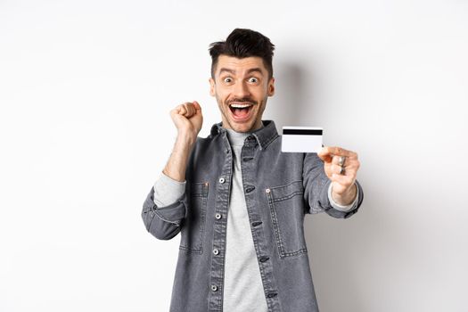 Happy man scream from excitement and show plastic credit card, recommending bank, standing on white background