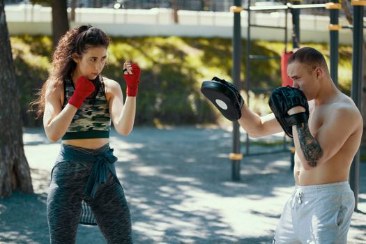 Boxers - muscular man and young woman engaged in boxing in the park ar sunny day