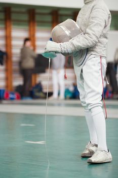 Participant of the fencing tournament with rapier and protective mask in hands