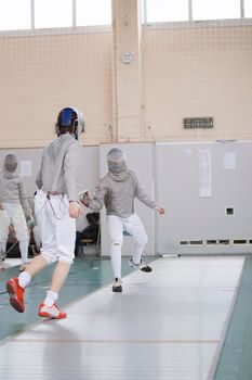 Young participants of the fencing tournament fighting in protective white clothes