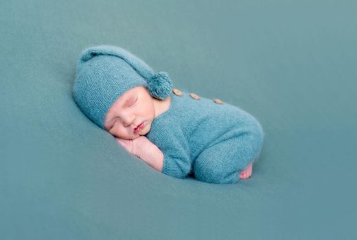 Infant baby boy sleeping in woolen costume with bare feet