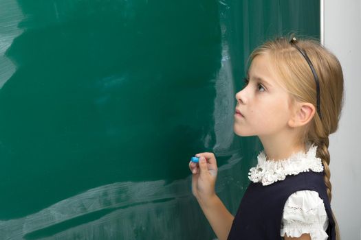 Adorable schoolgirl writing on green chalkboard