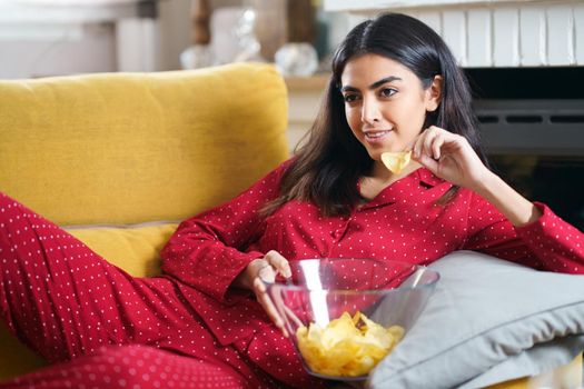 Persian woman at home watching TV eating chips potatoes