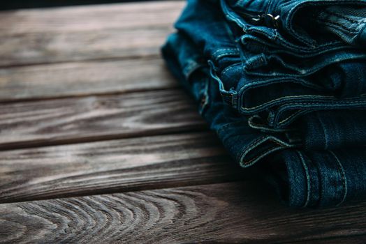 Stack of jeans pants on wooden table.