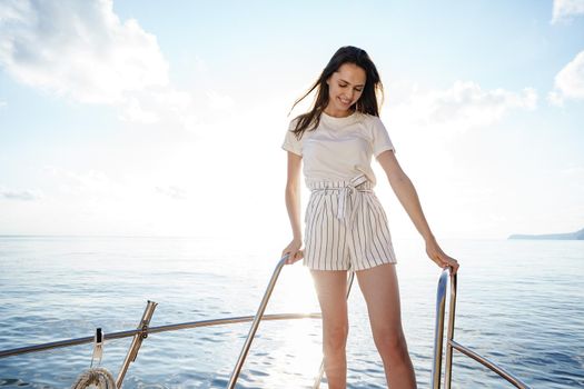 Young brunette woman standing on the nose of the yacht at a sunny summer day